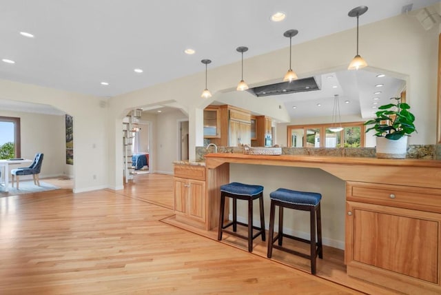 kitchen with decorative light fixtures, light wood-type flooring, a healthy amount of sunlight, and a kitchen bar