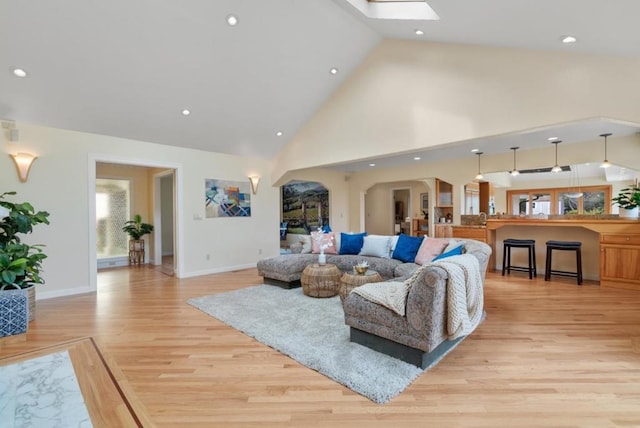 living room featuring light hardwood / wood-style flooring, high vaulted ceiling, and a skylight