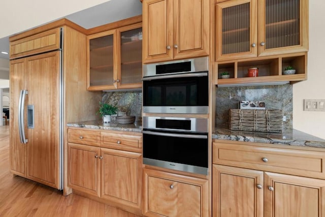 kitchen with paneled fridge, stainless steel double oven, backsplash, and light stone counters