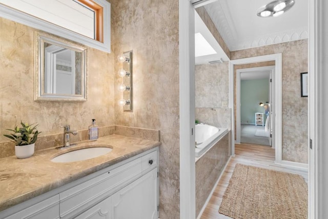 bathroom featuring hardwood / wood-style flooring, ornamental molding, vanity, and tiled tub