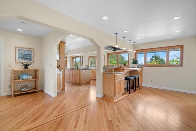 kitchen with a breakfast bar, hanging light fixtures, light brown cabinets, kitchen peninsula, and light hardwood / wood-style floors