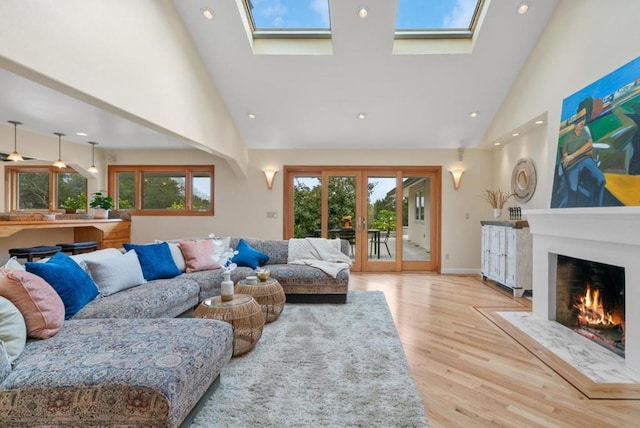 living room with light hardwood / wood-style floors, a skylight, and high vaulted ceiling