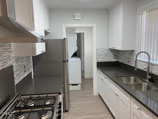 kitchen with wall chimney exhaust hood, sink, white cabinetry, range, and decorative backsplash