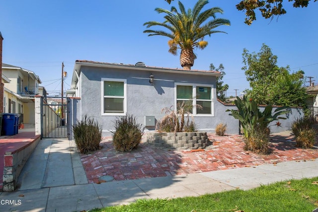 bungalow-style home with a gate, fence, and stucco siding