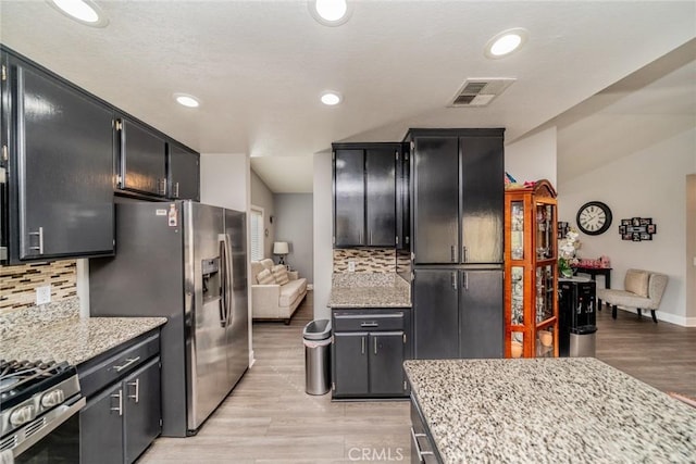 kitchen with backsplash, light hardwood / wood-style flooring, light stone countertops, and appliances with stainless steel finishes