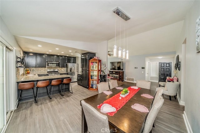 dining room featuring sink, light hardwood / wood-style floors, and vaulted ceiling