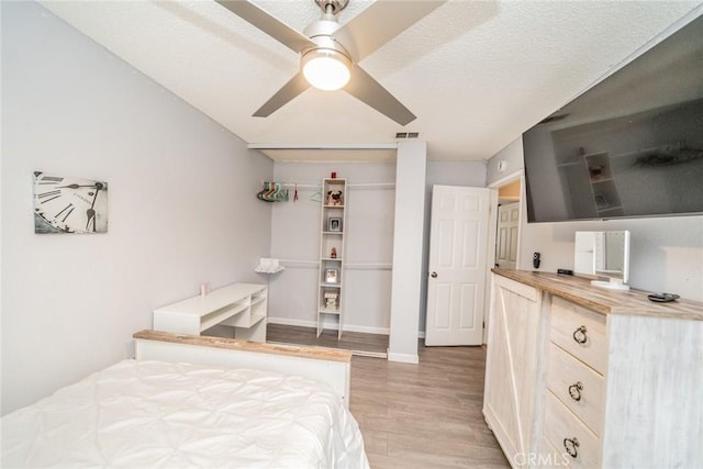 bedroom with light hardwood / wood-style floors, a textured ceiling, ceiling fan, and a closet