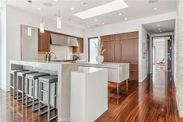 kitchen featuring wall chimney exhaust hood, decorative light fixtures, a skylight, dark hardwood / wood-style floors, and kitchen peninsula