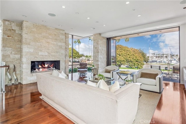 living room with floor to ceiling windows, a stone fireplace, and hardwood / wood-style floors