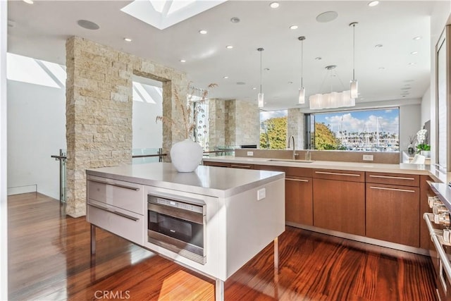 kitchen with pendant lighting, a skylight, sink, oven, and hardwood / wood-style flooring