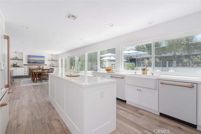 kitchen featuring white cabinetry, dishwasher, a kitchen island, and light wood-type flooring