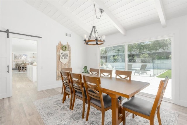 dining area with lofted ceiling with beams, a barn door, an inviting chandelier, and light hardwood / wood-style floors