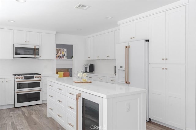 kitchen with white cabinets, beverage cooler, premium appliances, a center island, and light hardwood / wood-style flooring