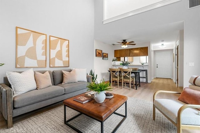 living room with light hardwood / wood-style flooring, ceiling fan, and a high ceiling