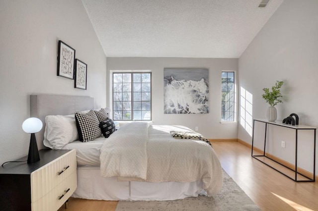 bedroom with lofted ceiling, a textured ceiling, and light hardwood / wood-style floors