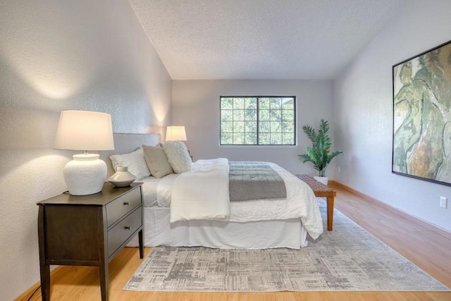 bedroom featuring lofted ceiling, a textured ceiling, and light hardwood / wood-style floors