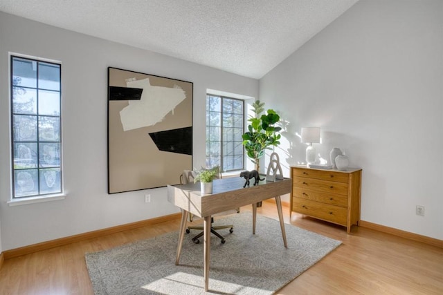 office space with vaulted ceiling, light hardwood / wood-style floors, and a textured ceiling