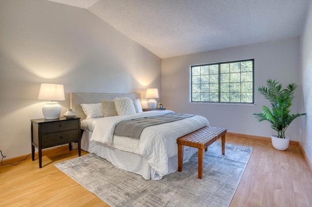 bedroom with vaulted ceiling, light hardwood / wood-style flooring, and a textured ceiling