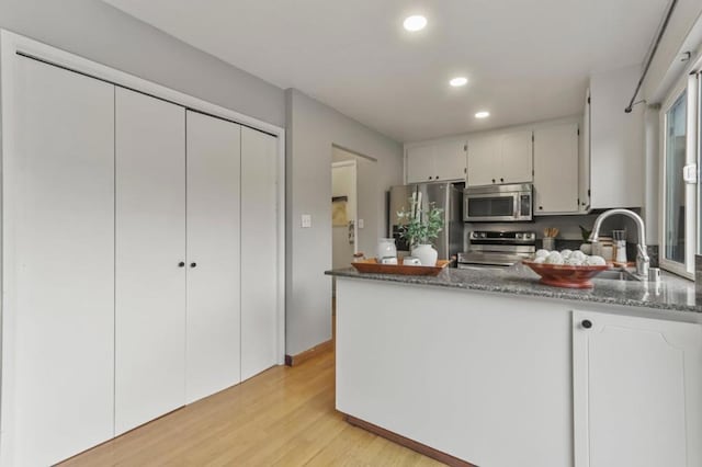 kitchen featuring dark stone countertops, appliances with stainless steel finishes, light wood-type flooring, and white cabinets