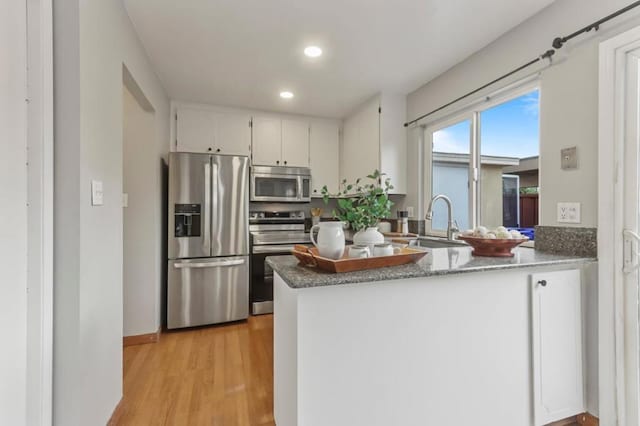 kitchen with sink, white cabinets, kitchen peninsula, stainless steel appliances, and light wood-type flooring