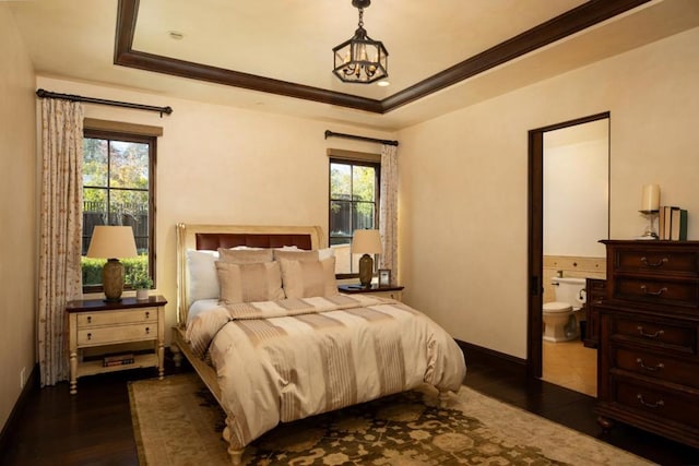 bedroom featuring dark wood-type flooring, connected bathroom, a raised ceiling, and crown molding