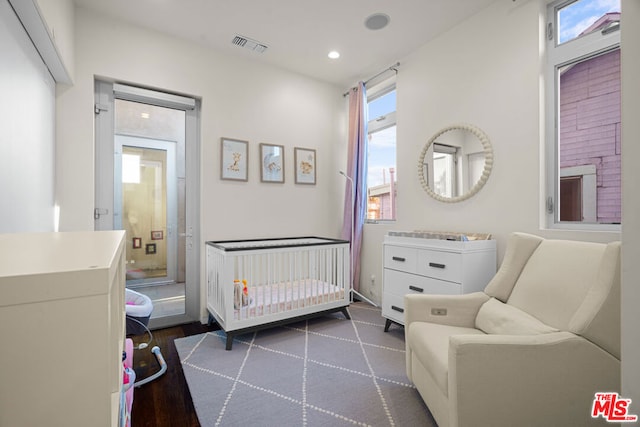 bedroom featuring a nursery area and dark hardwood / wood-style flooring