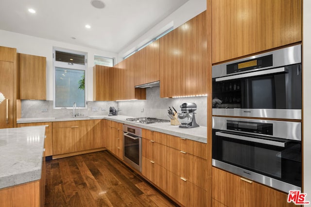 kitchen featuring sink, appliances with stainless steel finishes, dark hardwood / wood-style floors, light stone countertops, and decorative backsplash