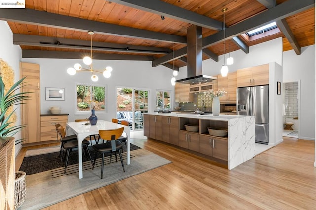 kitchen featuring pendant lighting, stainless steel fridge, a kitchen island, light brown cabinetry, and beamed ceiling