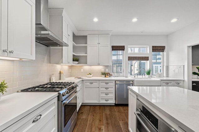 kitchen featuring appliances with stainless steel finishes, white cabinetry, backsplash, dark hardwood / wood-style floors, and wall chimney exhaust hood