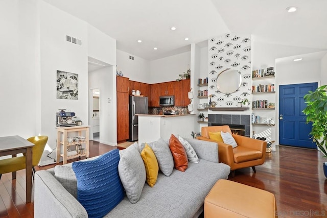 living room with a tiled fireplace, dark wood-type flooring, and high vaulted ceiling