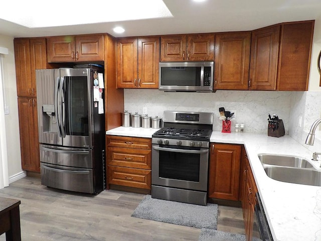 kitchen featuring appliances with stainless steel finishes, sink, backsplash, and light wood-type flooring