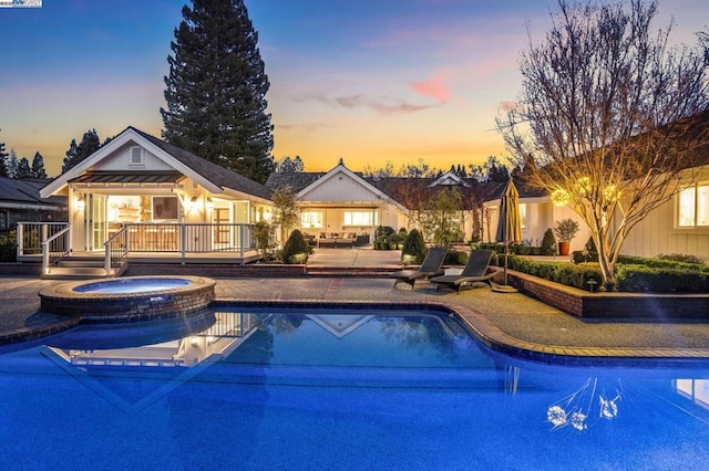 pool at dusk featuring a patio area and an in ground hot tub