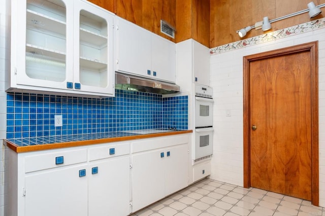 kitchen with cooktop, white cabinetry, tile counters, and white double oven