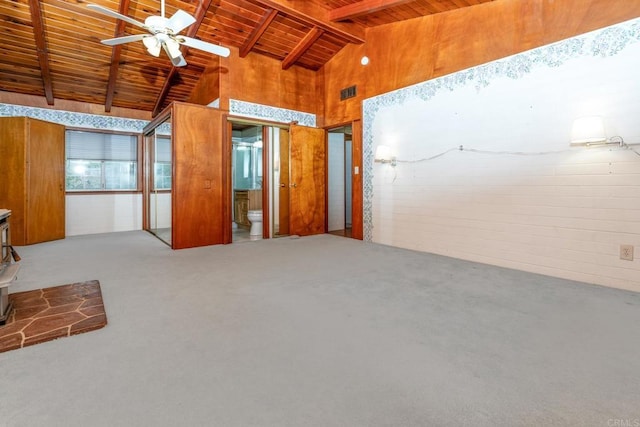 empty room with ceiling fan, carpet, lofted ceiling with beams, wooden ceiling, and a wood stove