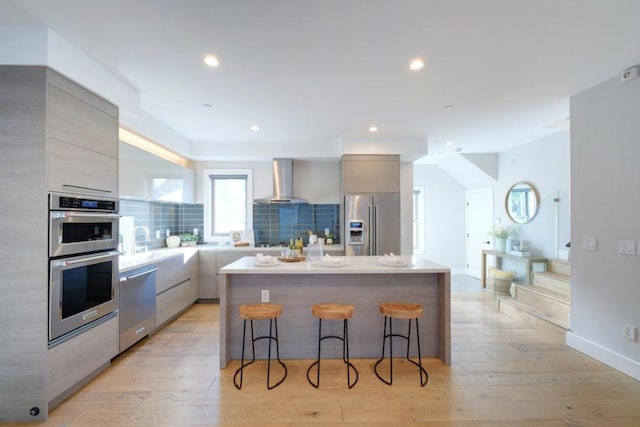 kitchen with a breakfast bar, tasteful backsplash, a center island, stainless steel appliances, and wall chimney range hood