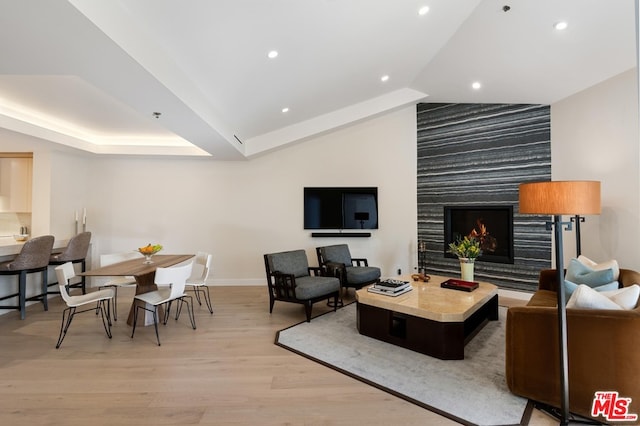 living room featuring a tray ceiling, light hardwood / wood-style floors, and a large fireplace