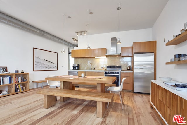 kitchen featuring stainless steel refrigerator, hanging light fixtures, light hardwood / wood-style floors, white range with gas cooktop, and wall chimney exhaust hood