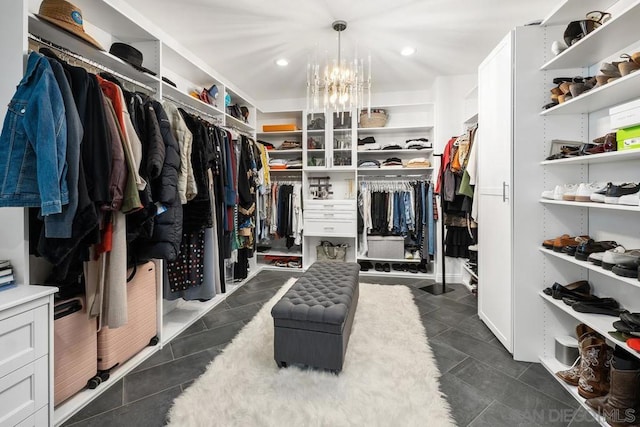 spacious closet featuring dark tile patterned flooring and an inviting chandelier