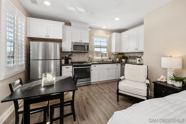 kitchen featuring sink, appliances with stainless steel finishes, white cabinetry, backsplash, and light hardwood / wood-style floors