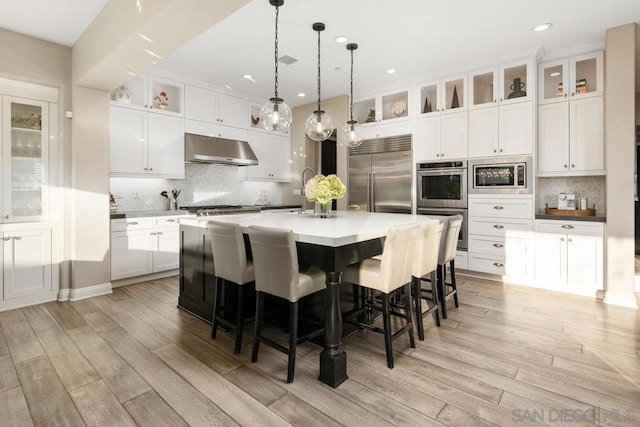 kitchen featuring pendant lighting, white cabinetry, built in appliances, and a kitchen island with sink