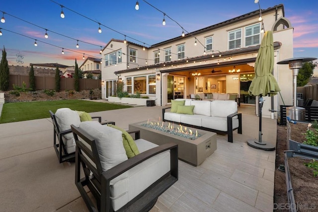 back house at dusk featuring a patio area and an outdoor living space with a fire pit