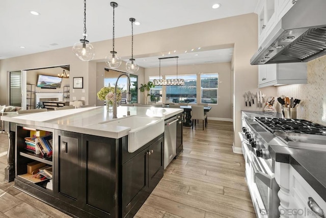 kitchen with pendant lighting, sink, appliances with stainless steel finishes, a kitchen island with sink, and white cabinets