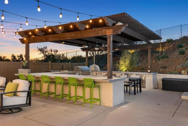 patio terrace at dusk featuring area for grilling, grilling area, ceiling fan, and exterior bar