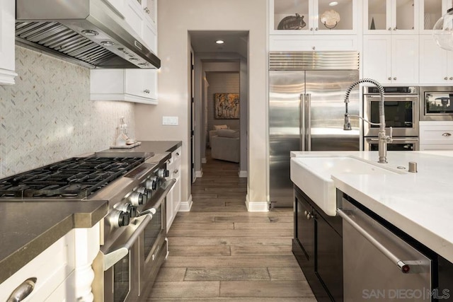 kitchen featuring tasteful backsplash, white cabinetry, wall chimney range hood, and built in appliances