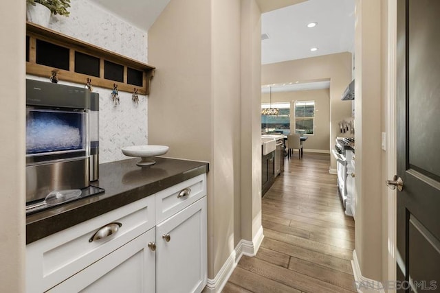 kitchen with range hood, light hardwood / wood-style floors, high end stove, and white cabinets