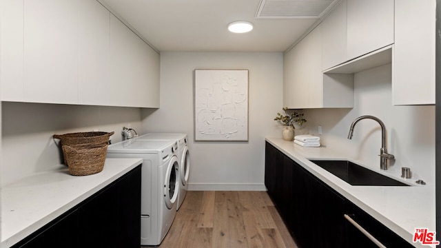 washroom featuring cabinets, sink, washing machine and dryer, and light wood-type flooring