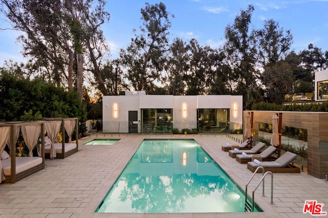 pool at dusk featuring an in ground hot tub and a patio