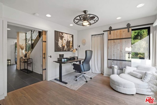 office space with a barn door, ceiling fan, and dark hardwood / wood-style flooring