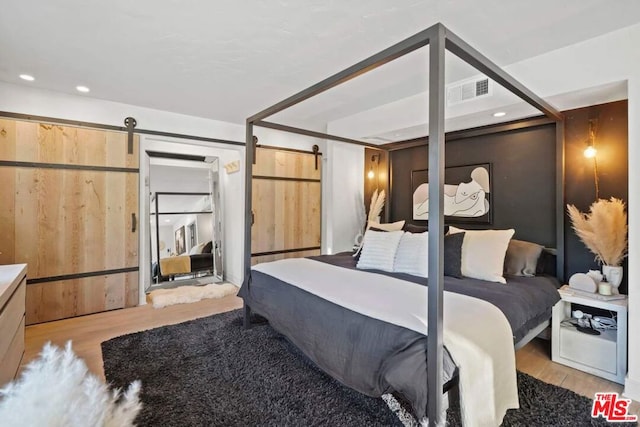 bedroom with a barn door and light hardwood / wood-style floors