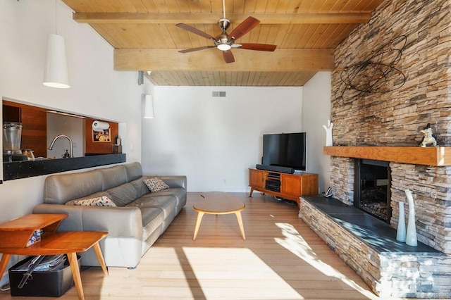 living room featuring beam ceiling, a stone fireplace, wooden ceiling, and ceiling fan